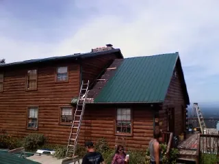 Green metal roof going on a two story log home with ladders set in Crab Orchard